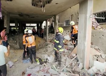 Firefighters and debris removal teams look at the destruction of a building in Gaza.